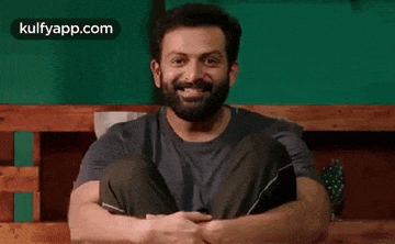 a man with a beard is sitting on a wooden bench with his legs crossed .