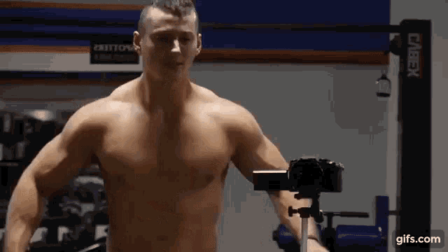 a shirtless man is taking a picture of himself in a gym with a camera .