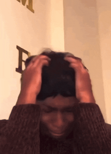 a man is holding his head in front of a wall with the letter f on it