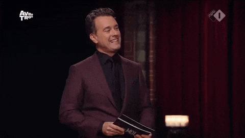 a man in a suit and tie is laughing on a stage while holding a book .