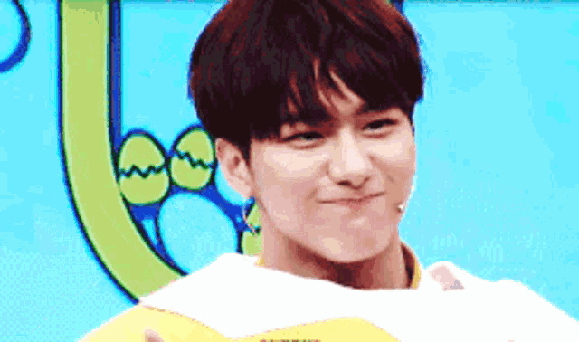 a young man is making a funny face while holding a yellow object in front of a blue background .