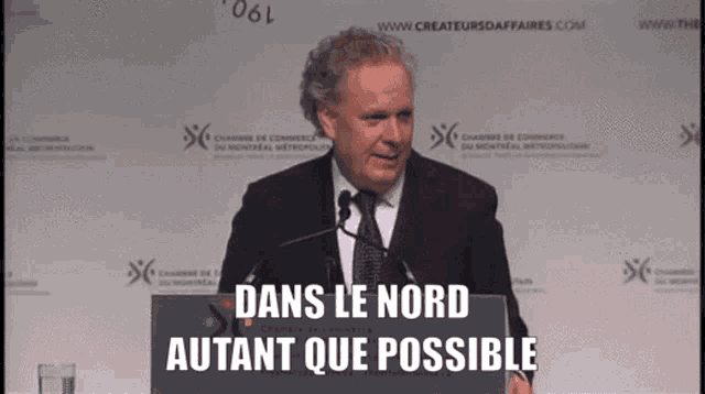 a man in a suit and tie stands at a podium with the words dans le nord autant que possible behind him