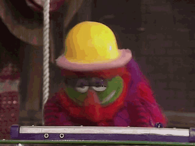 a clown wearing a yellow hard hat is sitting on a swing