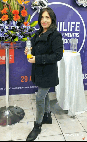 a woman holding a bottle of orange juice in front of a sign that says nillife
