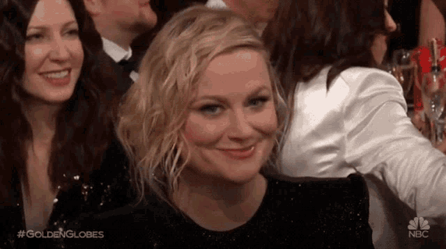 a woman is smiling while sitting in a crowd of people at a golden globes event .