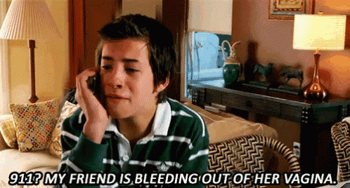 a young man is sitting on a couch talking on a cell phone and says 911 my friend is bleeding out of her vagina .