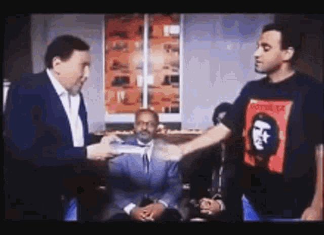 a man wearing a che guevara shirt is shaking hands with two other men