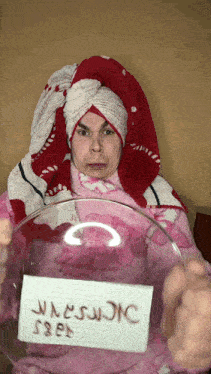 a man with a towel wrapped around his head is holding a glass bowl with a sign on it that says warning