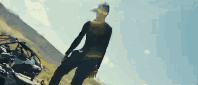 a man is standing on a hill next to a motorcycle .