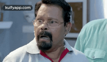 a man with glasses and a beard is making a funny face in a room .