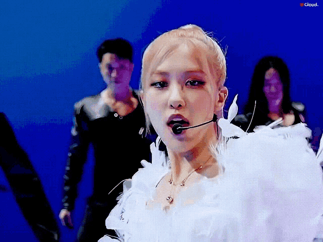 a woman wearing a white feathered dress and a microphone stands in front of a blue background