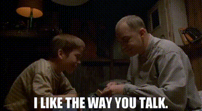 a man and a boy are sitting at a table and talking .