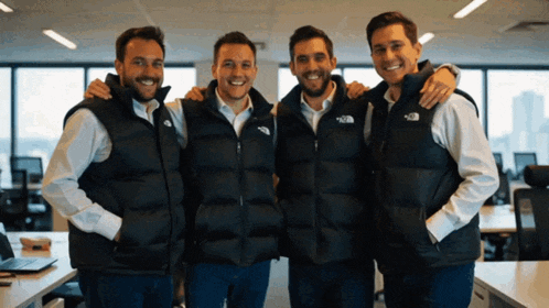four men wearing the north face vests are posing for a picture together