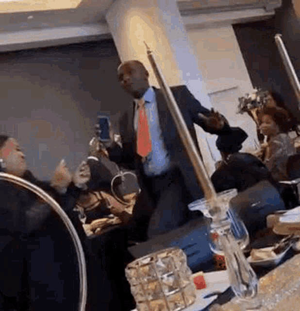 a man in a suit and tie is dancing in a room with people sitting at tables and candles .