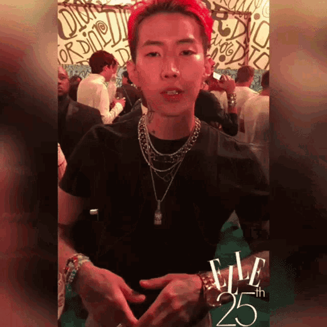a man with red hair is wearing a black t-shirt and silver necklaces