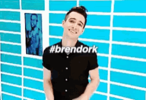 a man in a black shirt stands in front of a blue brick wall with #brendork written on it