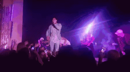 a man is singing into a microphone on a stage while a crowd watches .