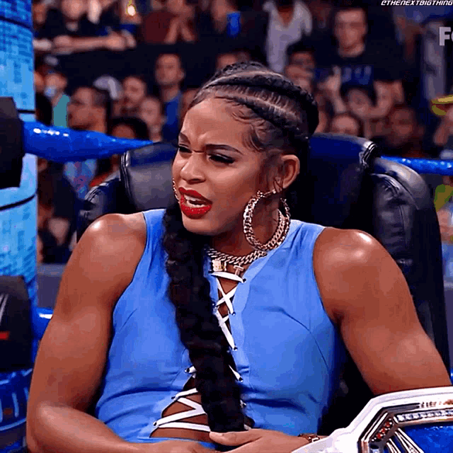 a woman in a blue top and hoop earrings sits in a chair with her mouth open