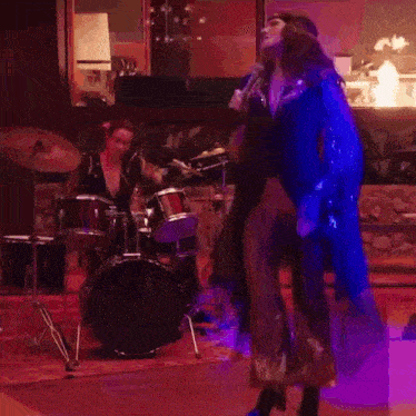 a woman is holding a microphone while dancing in front of a drum set ..