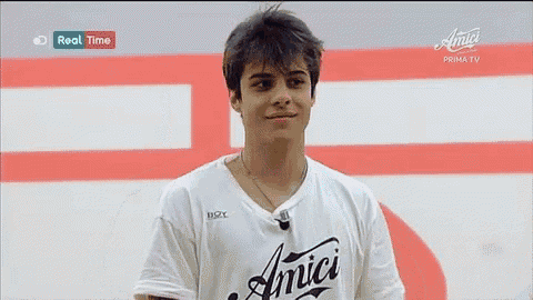 a young man wearing an amici t-shirt is standing in front of a red and white wall