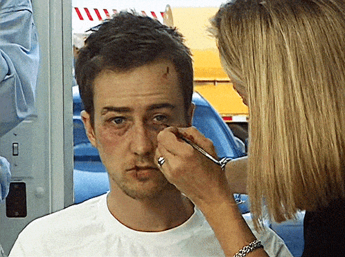a woman is applying makeup to a man 's face with a brush