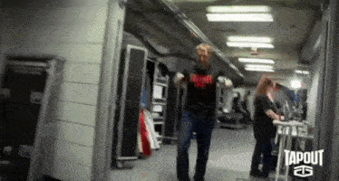 a man in a tapout shirt is dancing in a dark hallway