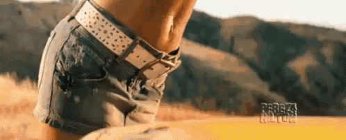 a woman wearing shorts and a belt is standing in a field with mountains in the background .