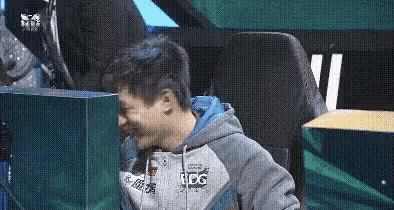 a man in a hoodie is sitting in a chair in front of a computer screen .