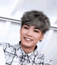 a young man with gray hair is smiling while wearing a plaid shirt .