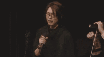 a man wearing glasses is holding a microphone in his hand .