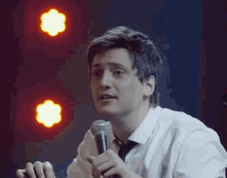 a man in a white shirt and tie is holding a microphone in his hand .