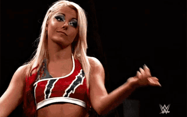 a woman in a red and white top is standing in a wrestling ring and smiling .