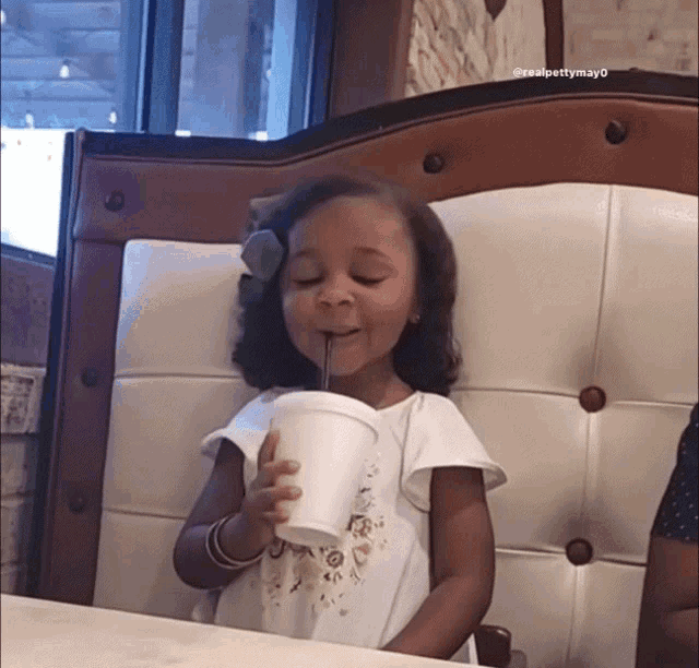 a little girl drinking through a straw from a white cup
