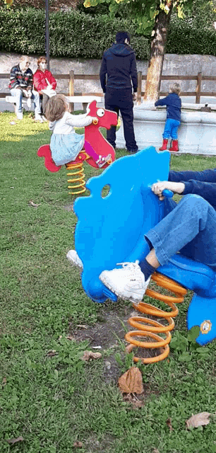 a group of children are playing on a blue and red rocking horse