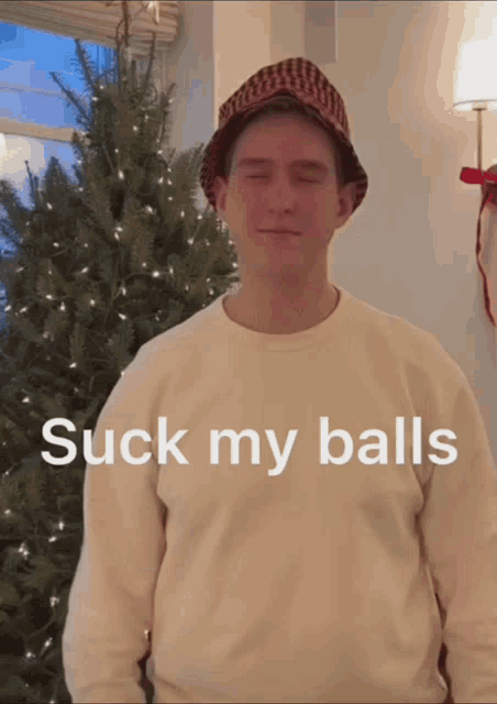 a man standing in front of a christmas tree with the words " suck my balls " on the front of his shirt