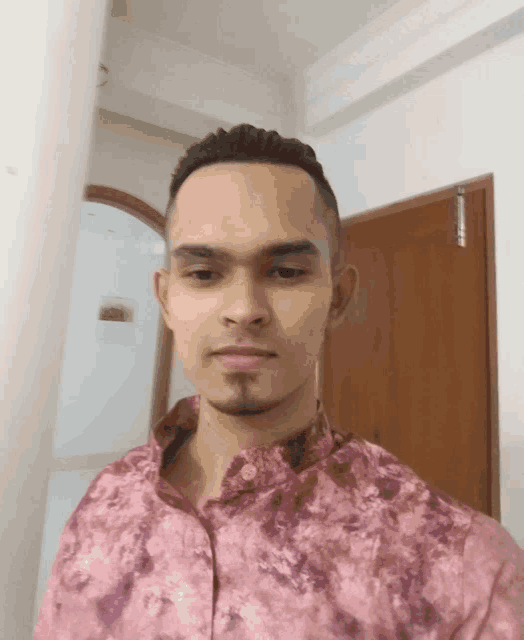 a man wearing a pink shirt is standing in front of a door