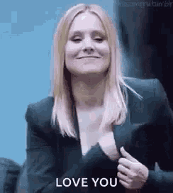a woman in a black suit is smiling and holding her breast while saying `` love you '' .
