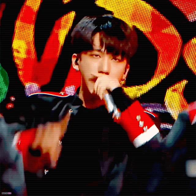 a young man is singing into a microphone with a colorful background