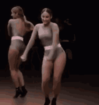 a woman is dancing on a stage in a dark room while a man watches .