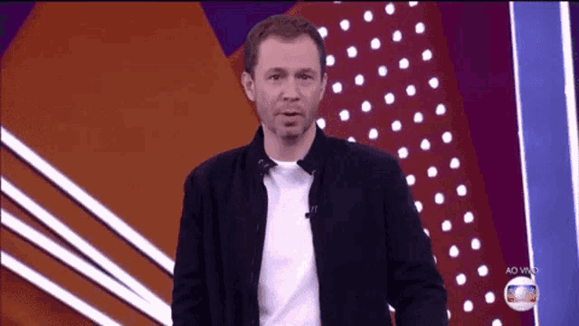 a man in a black jacket and white shirt is standing in front of a polka dot background .
