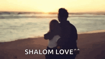 a man and a woman are hugging each other on the beach at sunset .