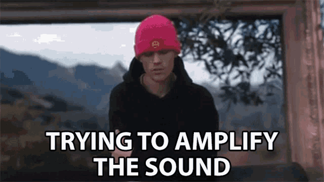 justin bieber is wearing a pink beanie and a black hoodie while standing in front of a window .