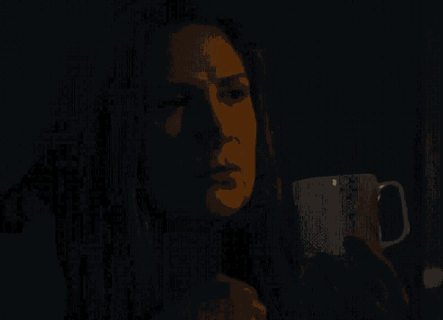 a woman in a dark room holds a white cup