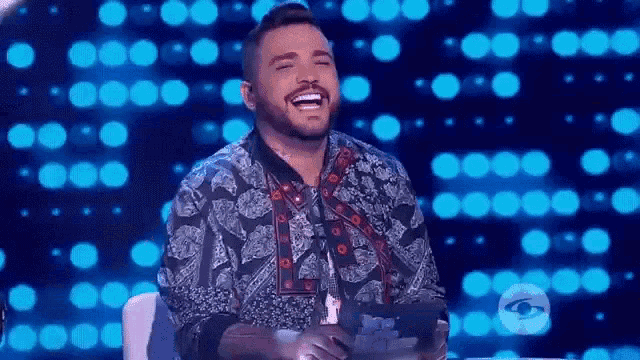 a man with a beard is sitting in a chair and laughing on a stage .
