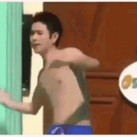 a shirtless man in blue shorts is standing in front of a door in a room .