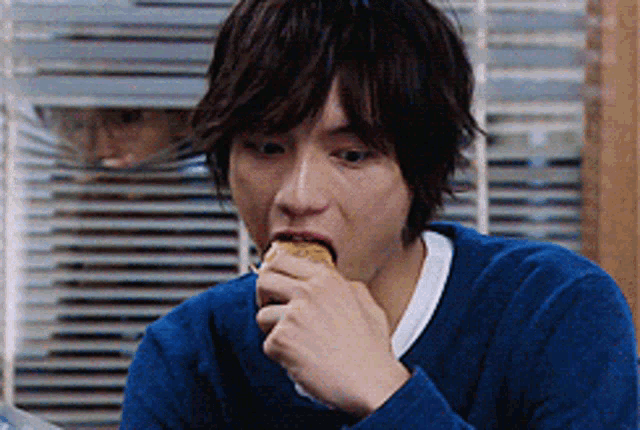 a man wearing a blue sweater is eating a sandwich