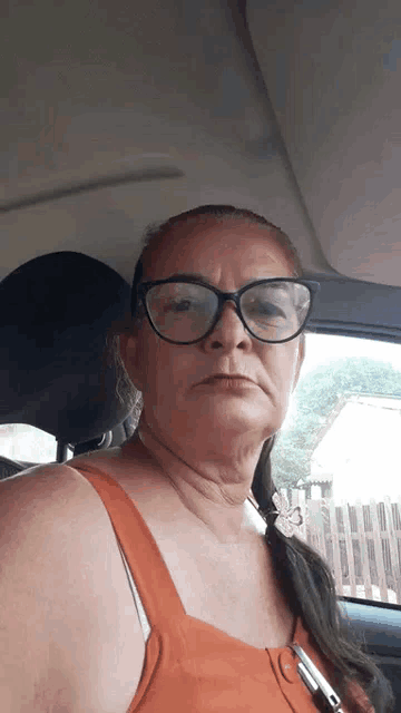 a woman wearing glasses is sitting in a car with a pen in her pocket .