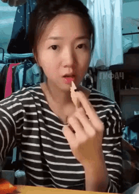 a woman in a striped shirt is eating a piece of food with her hands .