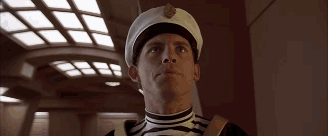 a man in a white hat is standing in a hallway with the word tall behind him