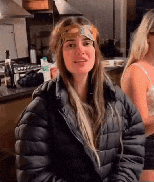a woman wearing a mask and a jacket is sitting in a kitchen